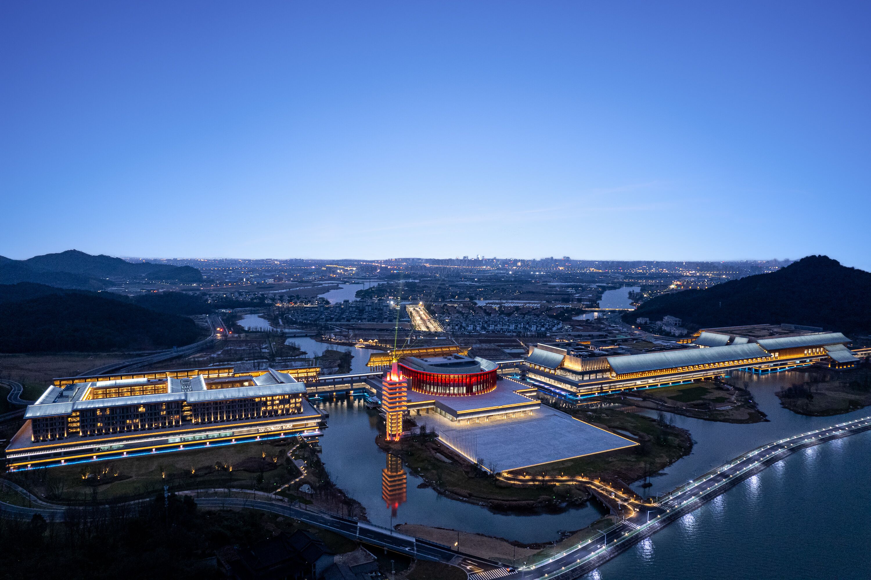Une vue aérienne d’un complexe moderne composé de plusieurs bâtiments, avec une grande structure centrale et une rivière.