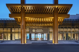Entrada de hotel con diseño moderno, que incluye un dosel de madera y puertas de cristal.
