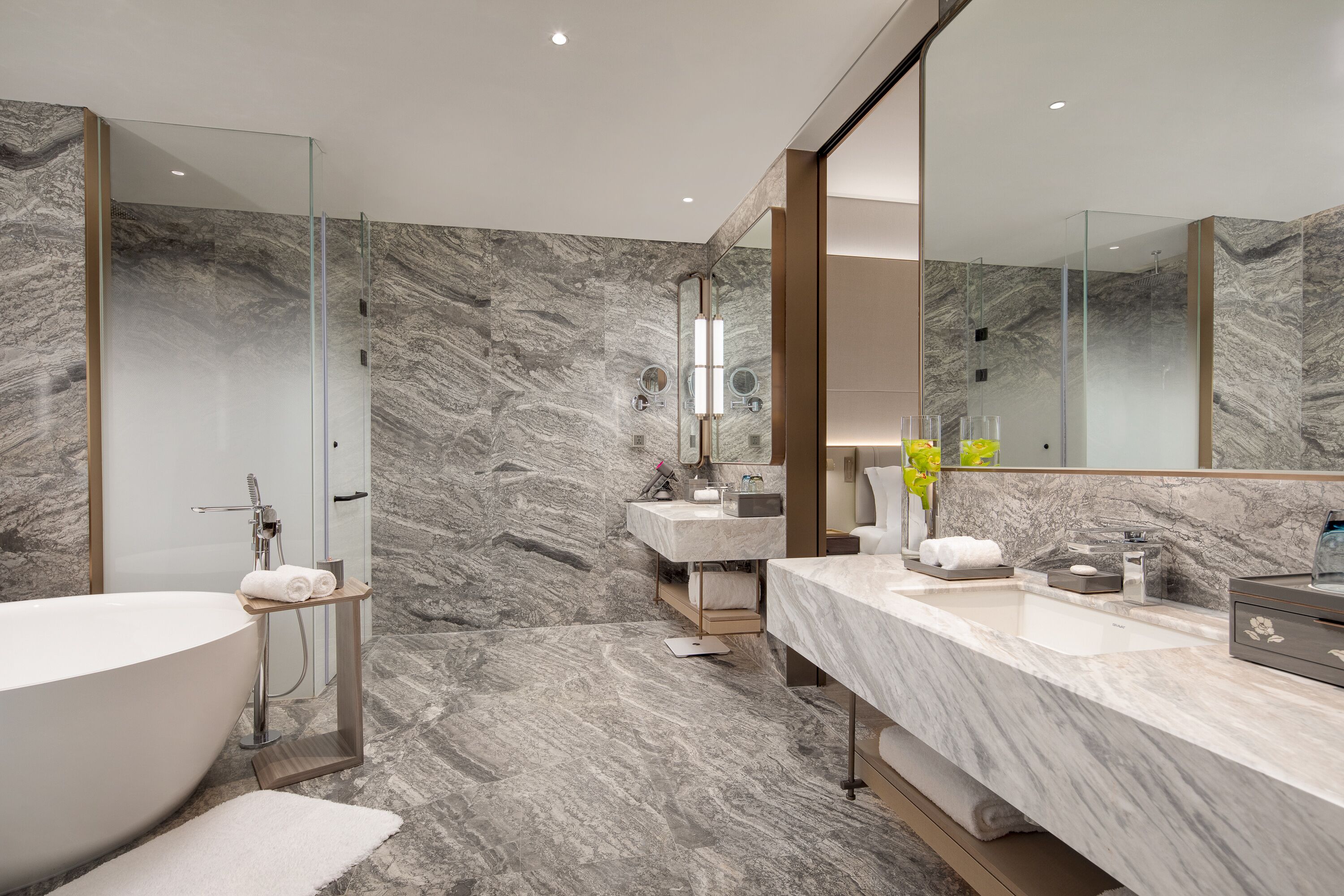 A modern bathroom with a freestanding bathtub, a large mirror, and a marble backsplash.