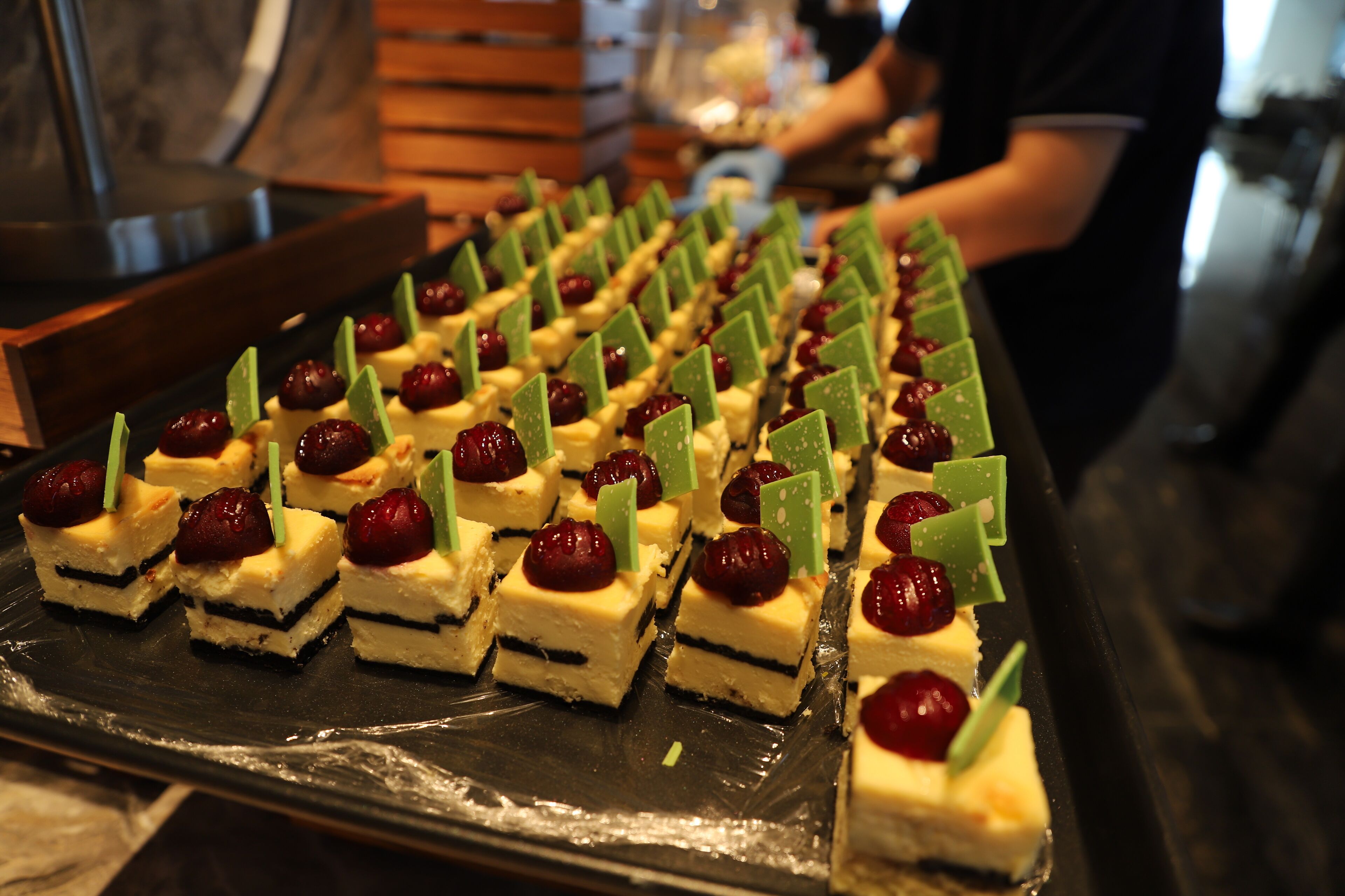 A tray of dessert cubes with cherries and green decorations.