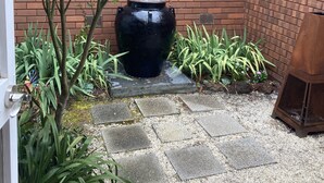 Ein Innenhof mit einem großen schwarzen Wasserspiel, einer Ziegelwand und verschiedenen Pflanzen.