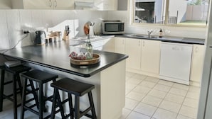 Une cuisine moderne avec des meubles blancs, un grand îlot central doté de tabourets, un four à micro-ondes et un lave-vaisselle.