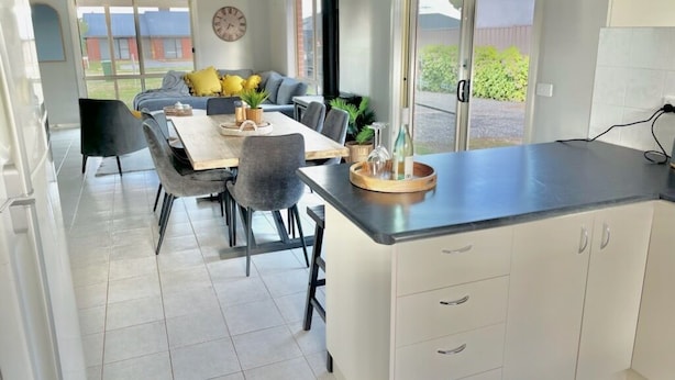 Une cuisine moderne avec des meubles blancs, un plan de travail noir et un coin repas comprenant une table et des chaises.