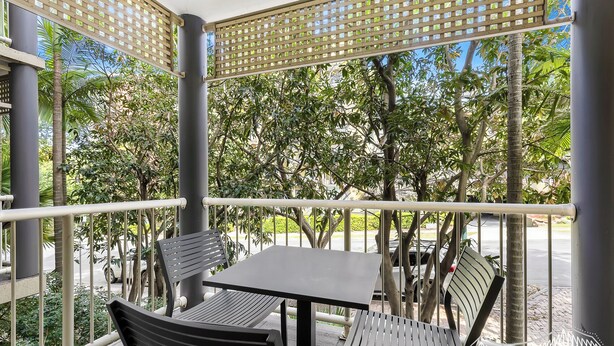 An outdoor seating area with a table and chairs, surrounded by a wooden lattice structure and greenery.