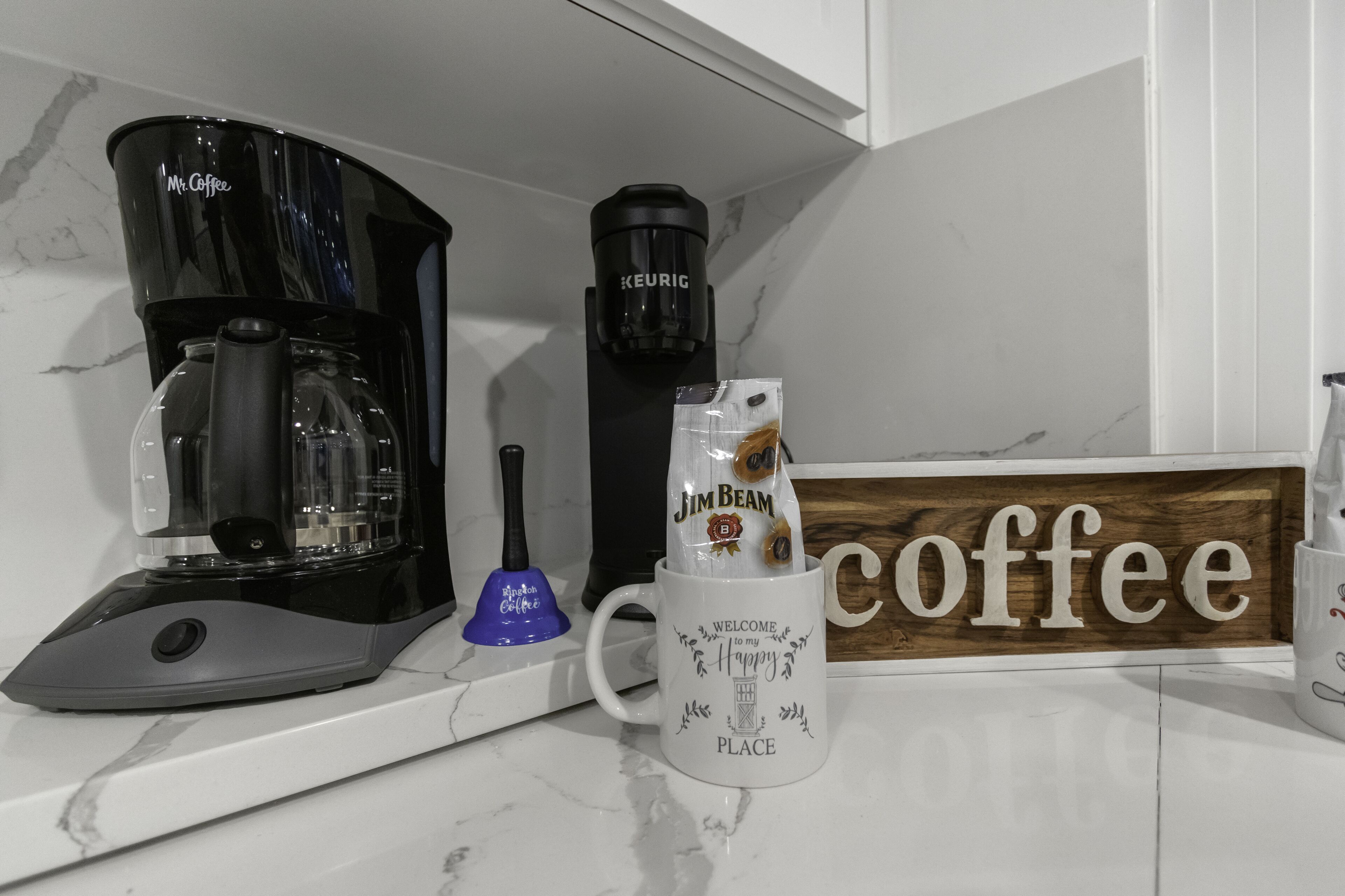 A coffee maker, a Keurig coffee pod dispenser, a coffee mug, and a wooden sign that says "Coffee".