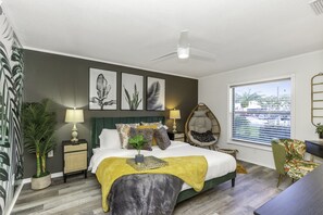 A modern bedroom with a bed, bedside tables, a ceiling fan, a window with blinds, and a view of the city. - Tropical 5BR Pool Beach House - 5min from Beaches! (Seminole)