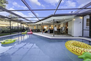 A covered outdoor swimming pool with inflatable toys, a patio area, and a view of the house. - Tropical 5BR Pool Beach House - 5min from Beaches! (Seminole)