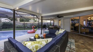 A modern outdoor living area with a sofa, cushions, and a pool. - Tropical 5BR Pool Beach House - 5min from Beaches! (Seminole)