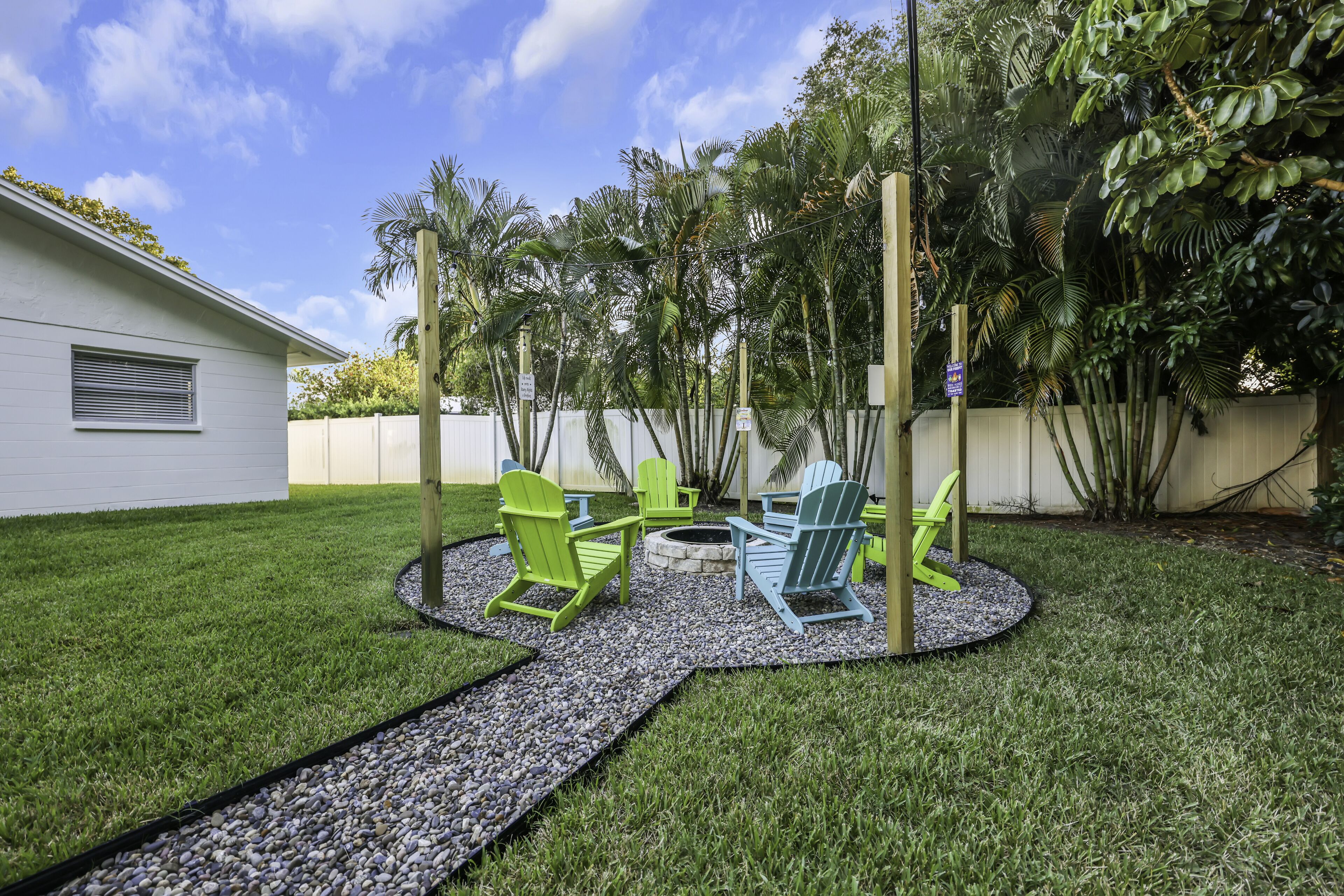 A backyard with a fire pit, green Adirondack chairs, and a white building.