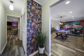 A living room with a pool table, a vibrant floral wall, and a wooden floor. - Tropical 5BR Pool Beach House - 5min from Beaches! (Seminole)