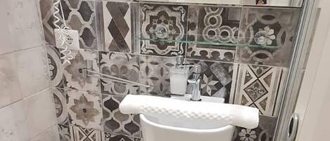 A bathroom with a white toilet, a white sink, and a mirror. The walls are tiled with various patterns.