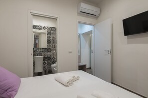 A hotel room with a bed, a TV, an air conditioner, and a bathroom visible through an open door. - Bed&BikeRome Giulio Cesare (Rome)