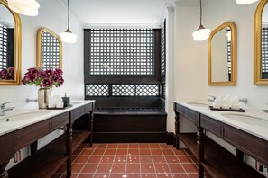 Een badkamer met twee wastafels, een bankje en een latticestraalvenster.