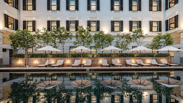 Une cour d’hôtel avec une piscine, des chaises longues, des parasols et des arbres.