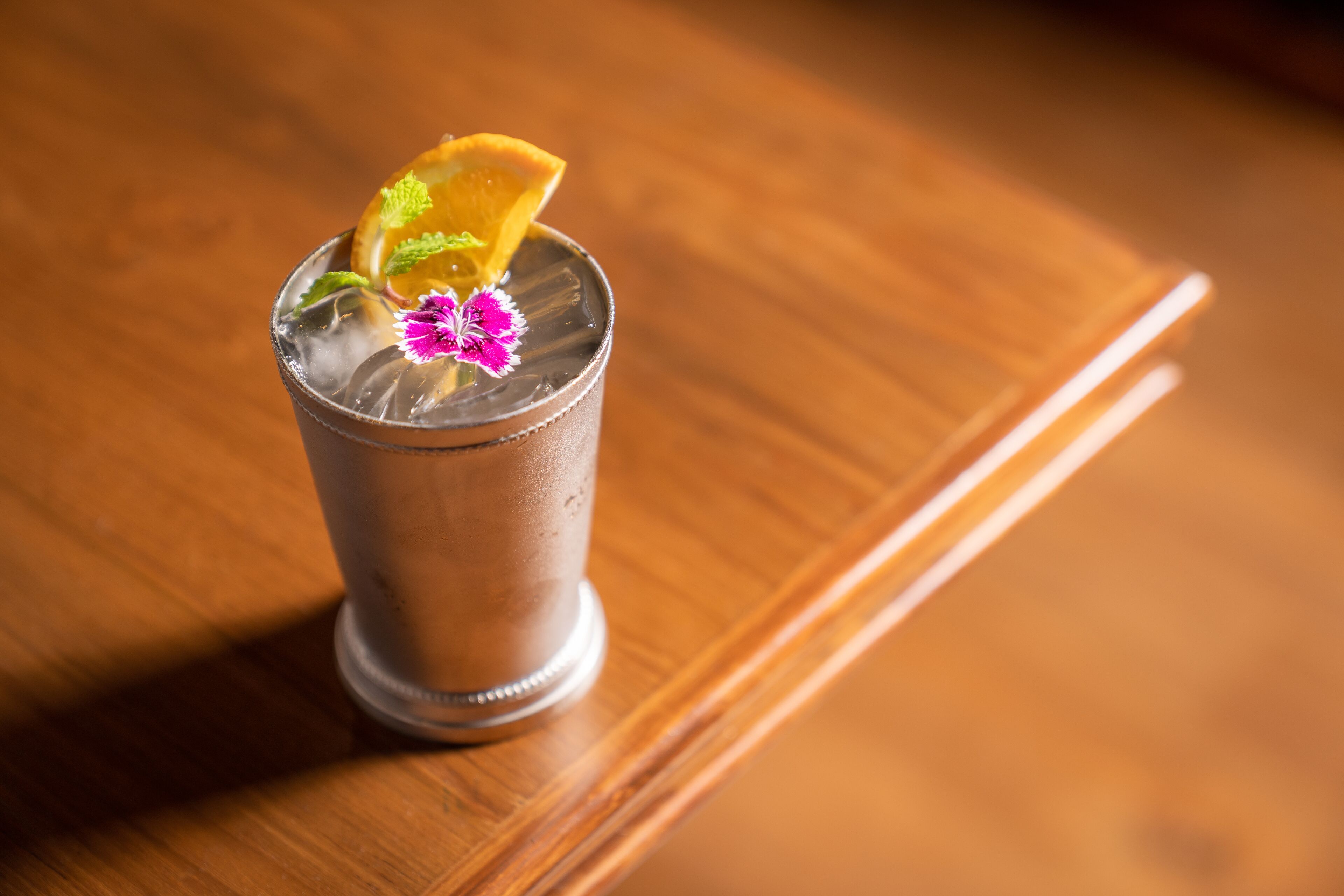 A glass with a beverage, garnished with a slice of fruit and a flower, on a wooden surface.
