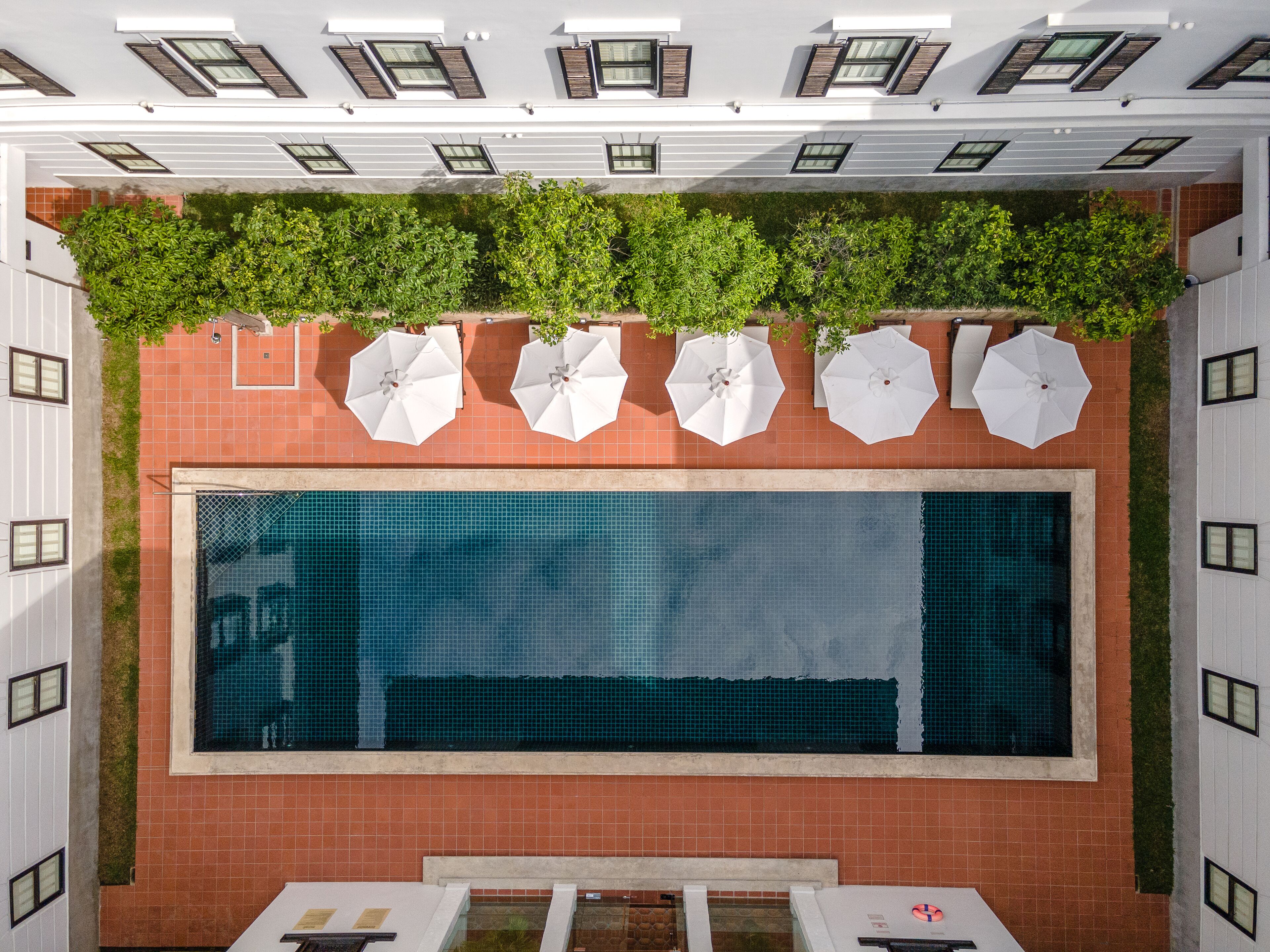 A rooftop pool with a tiled floor, surrounded by white umbrellas and greenery.