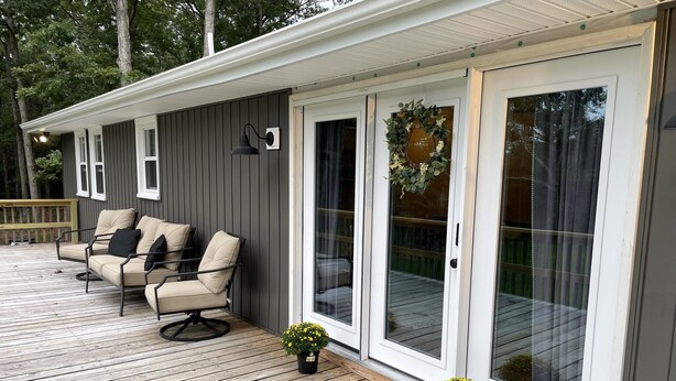 A covered deck with a sofa and chairs, a potted plant, and a sliding glass door with a wreath.