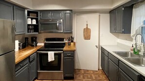 A modern kitchen with dark cabinets, stainless steel appliances, and a wooden floor.