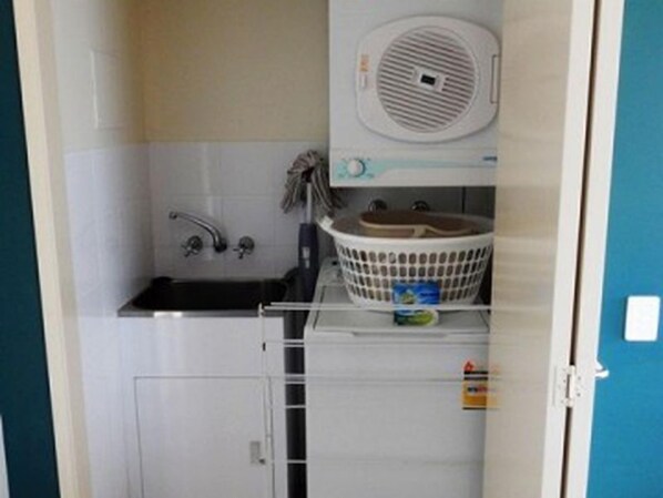 A compact bathroom with a sink, a small laundry basket, and a toilet.