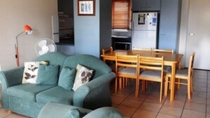En kompakt opholdsstue med sofa, spisebord og tekøkken.