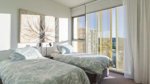 Moderni hotellihuone, jossa on kaksi sänkyä, suuri ikkuna verhoilla ja näkymä kaupunkiin.