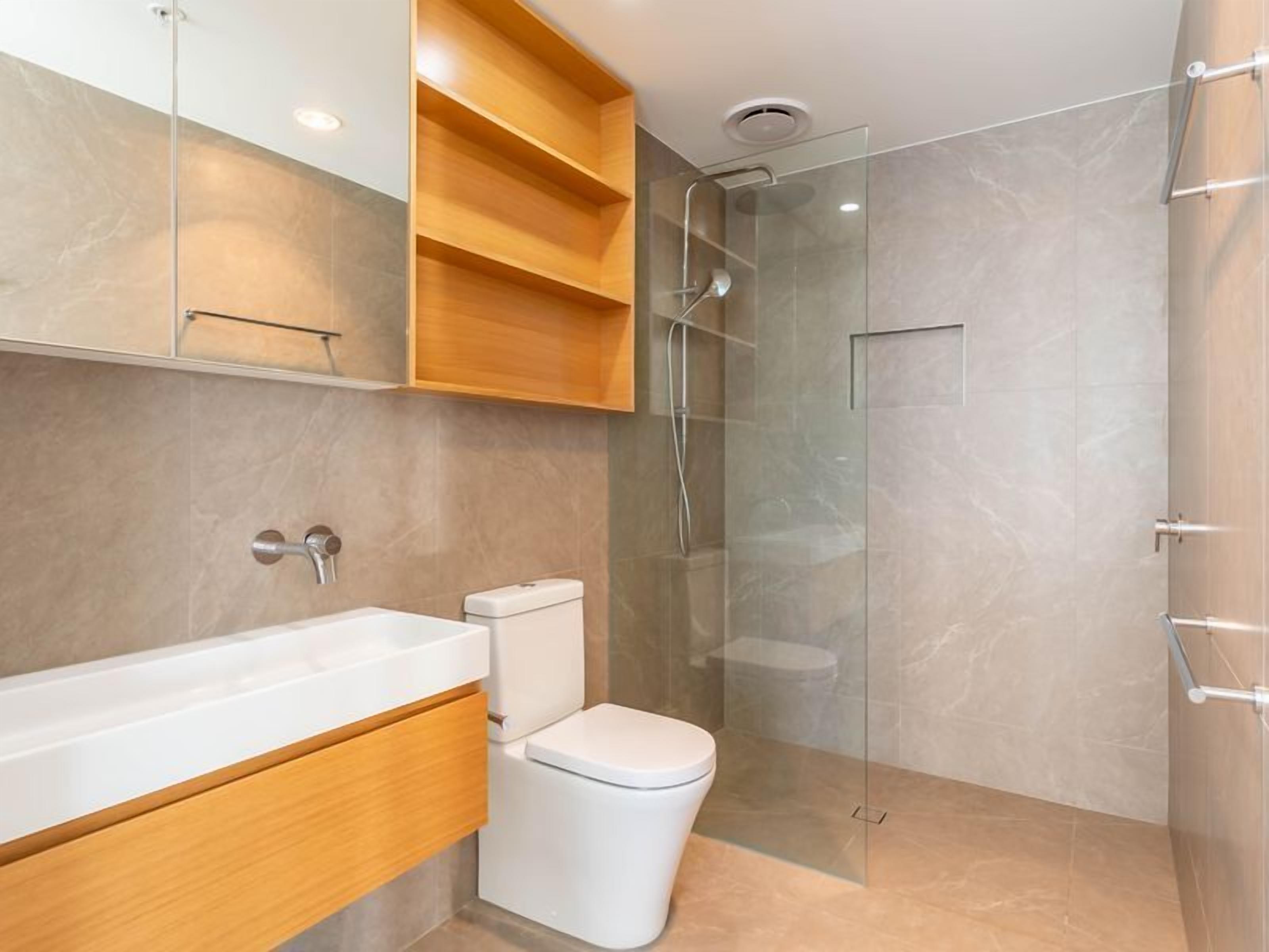 A modern bathroom with a glass-enclosed shower, a white toilet, and a wooden vanity with a mirror.