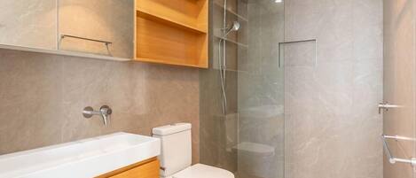 A modern bathroom with a glass-enclosed shower, a white toilet, and a wooden vanity with a mirror.