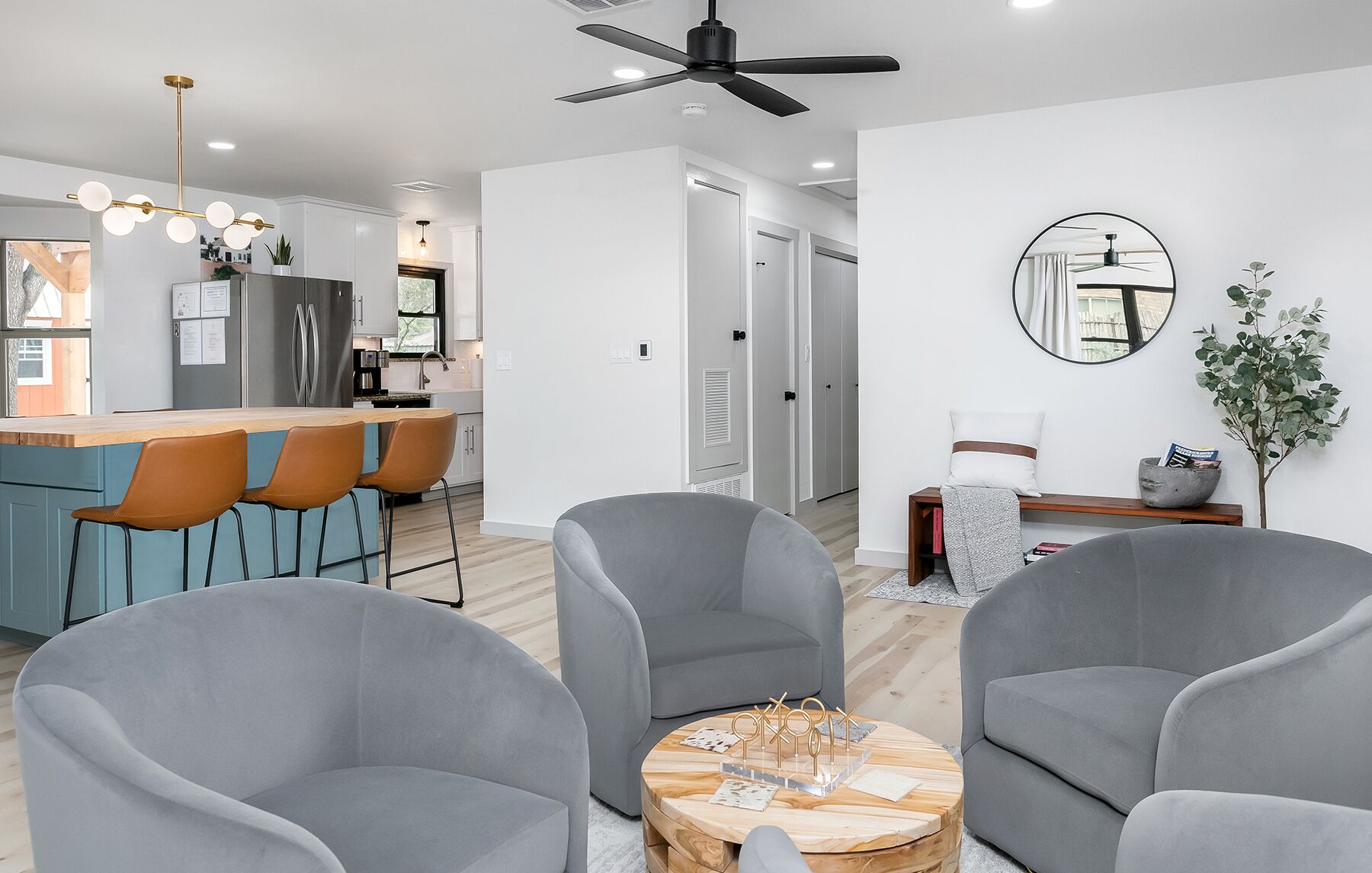 Een moderne woonkamer met grijze fauteuils, een houten salontafel en een keuken met een bar en zitplaatsen.