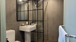 Een moderne badkamer met een glazen douchecabine, een wit toilet en een wastafel met spiegel.