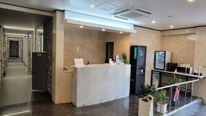 Een moderne hotelentree met een receptiebalie, een trap en een gang naar de kamers.