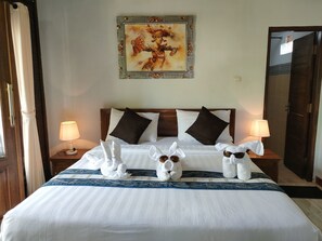 Una habitación de hotel con una cama bien hecha, dos lámparas de noche, una obra de arte enmarcada sobre la cama y una puerta de madera a la derecha.