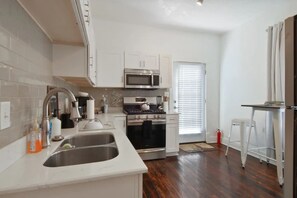 A modern kitchen with white cabinets, stainless steel appliances, and a large window. - Courtney on Second | Garden District Getaway (New Orleans)