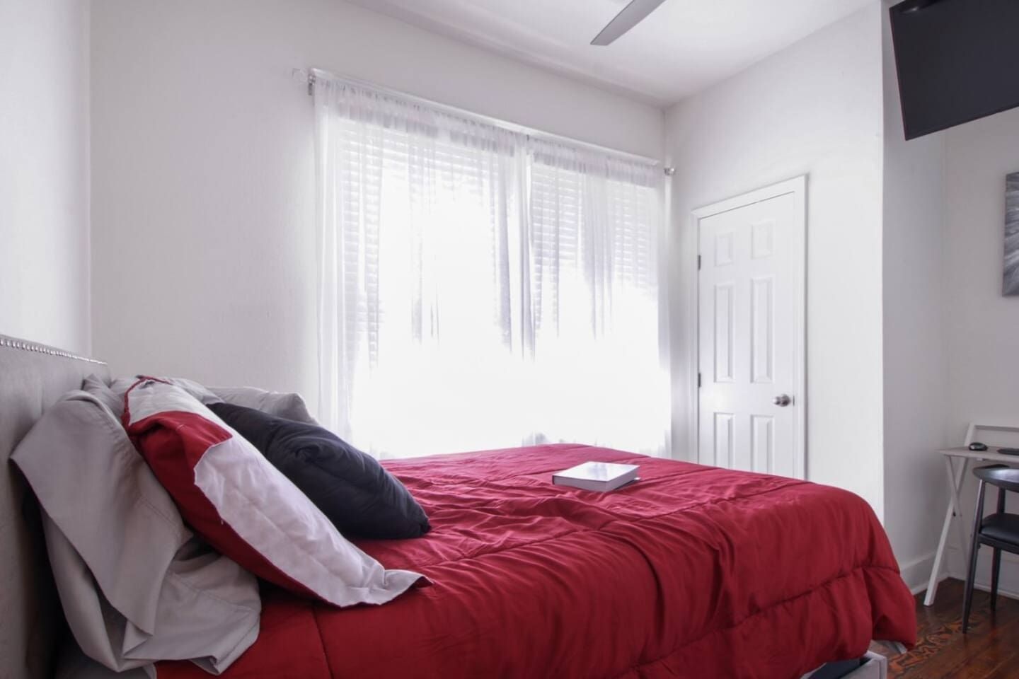 A bedroom with a bed, a window with curtains, a door, and a desk with a chair.