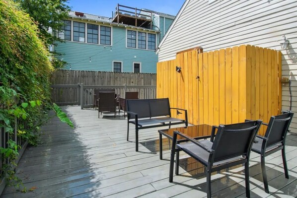 An outdoor patio area with a wooden deck, metal chairs, and a wooden fence.