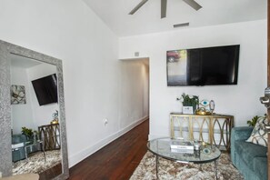 A modern living room with a flat-screen TV mounted on the wall, a glass coffee table, and a sofa.