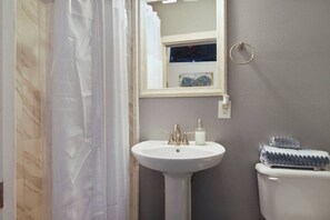 A bathroom with a white pedestal sink, a toilet, and a shower curtain. - Courtney on Second | Garden District Getaway (New Orleans)