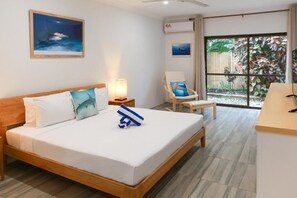 A hotel room with a bed, a chair, a desk, and a large window with a view of greenery.