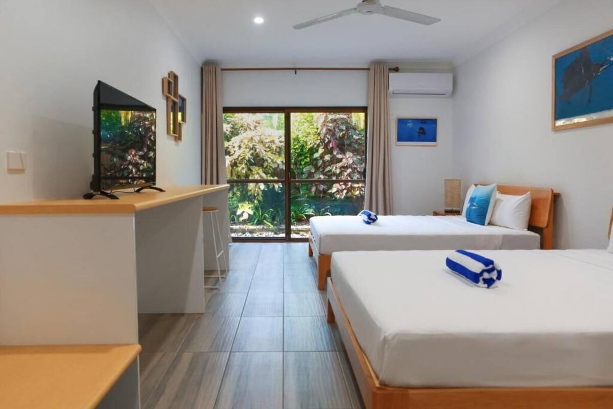 A hotel room with two beds, a desk, a television, and a sliding glass door to a balcony.