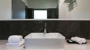 A modern bathroom with a white sink, dark tiled walls, and a large mirror. - Birch Resort Port Douglas (Port Douglas)