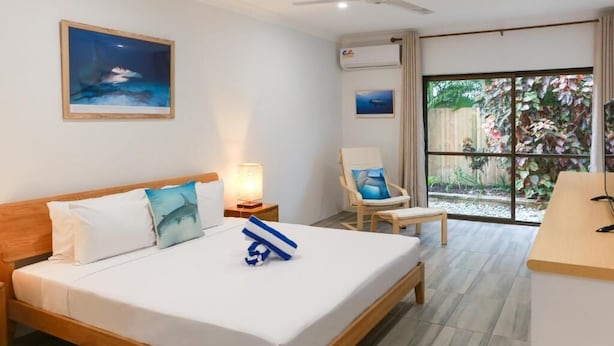 A hotel room with a bed, a chair, a desk, and a window with a view of a garden. - Birch Resort Port Douglas (Port Douglas)