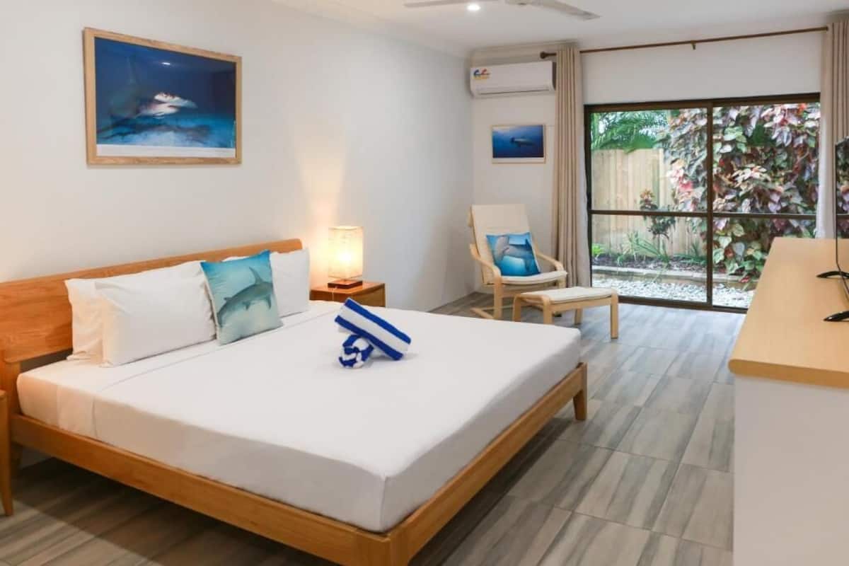 A hotel room with a bed, a chair, a desk, and a window with a view of a garden.
