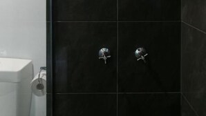 A modern bathroom with black tiles, a glass shower enclosure, and a white toilet. - Birch Resort Port Douglas (Port Douglas)