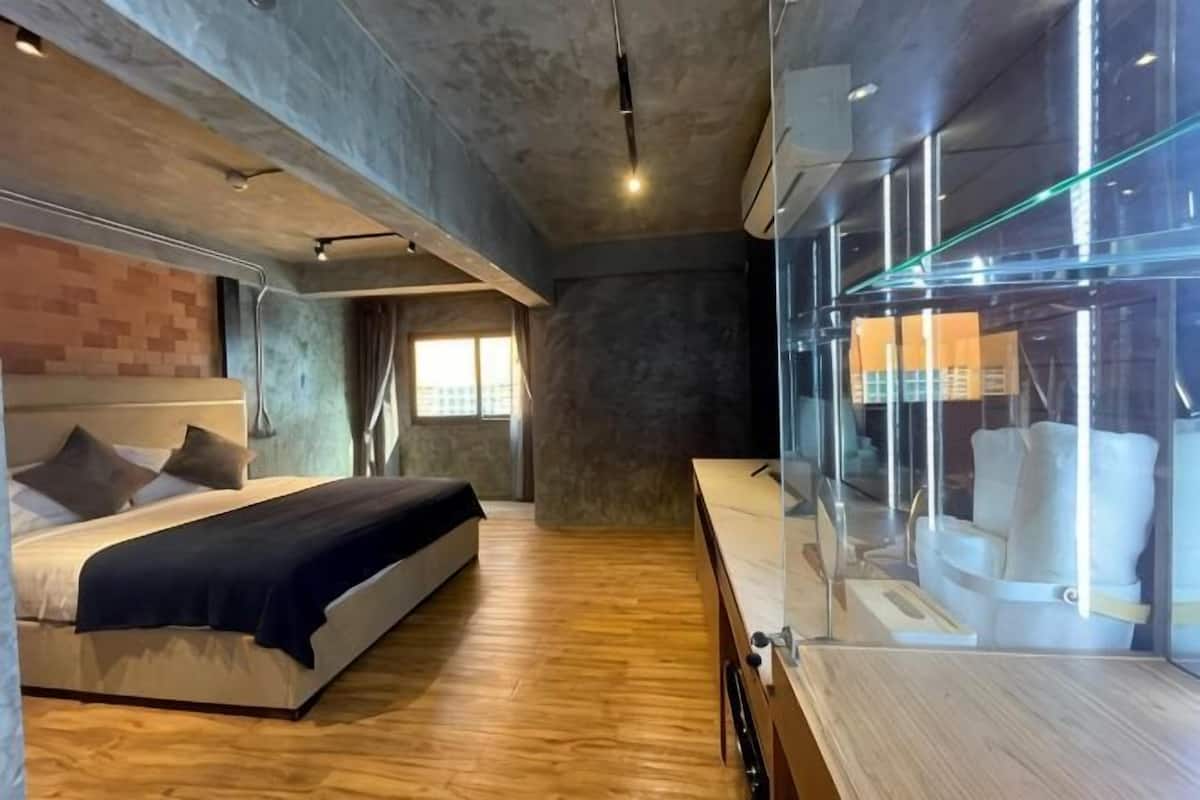 A modern bedroom with a bed, wooden flooring, a glass partition, and a view of the city.