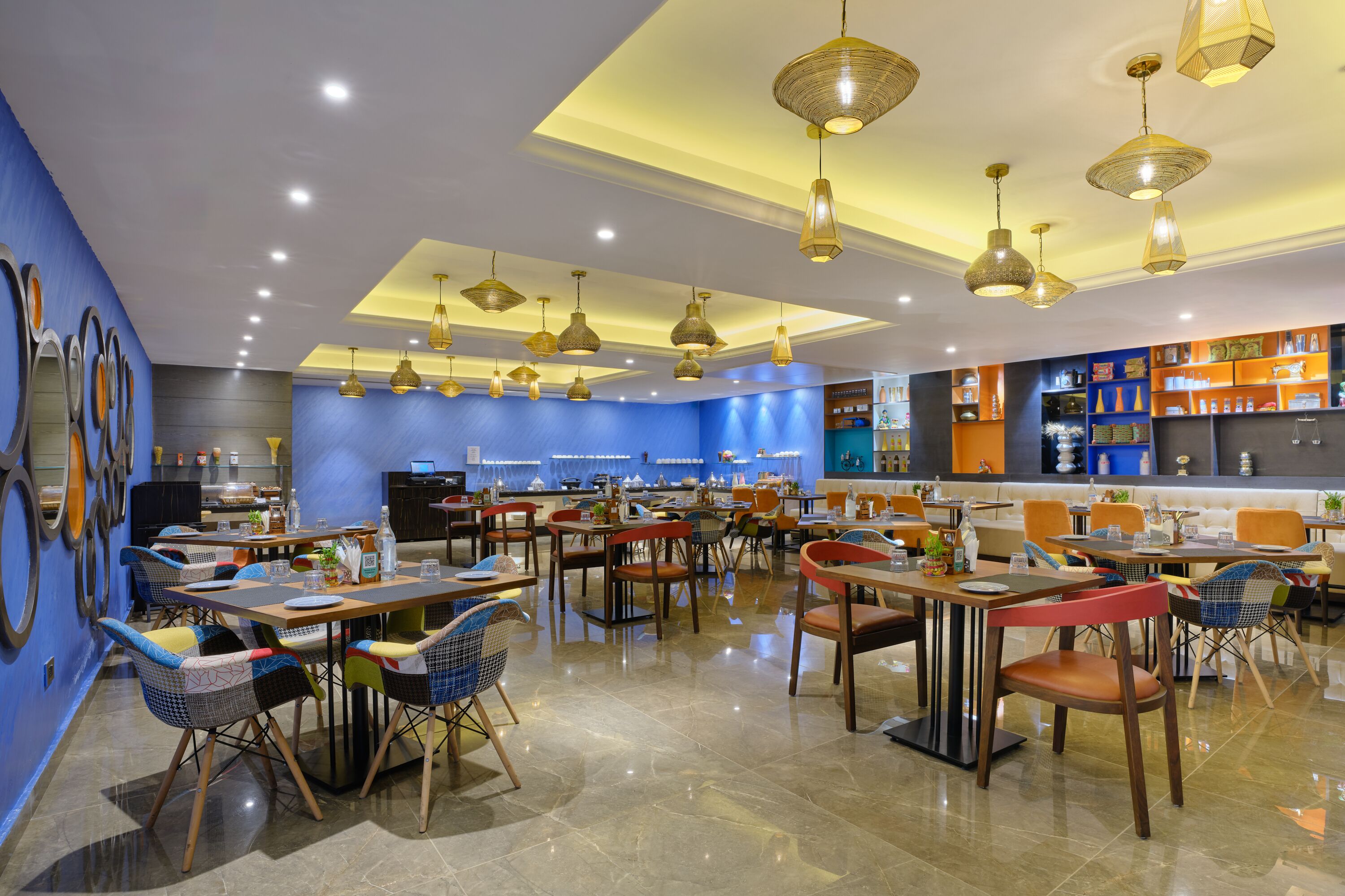 Un restaurante moderno con varias mesas y sillas, iluminación colgante y una pared azul de acento.