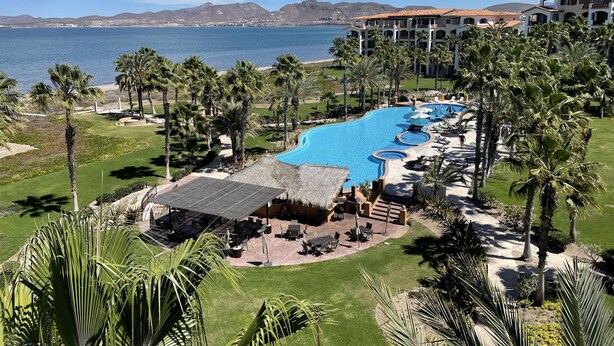 Ein Resort mit großem Schwimmbad, Palmen und Meerblick.