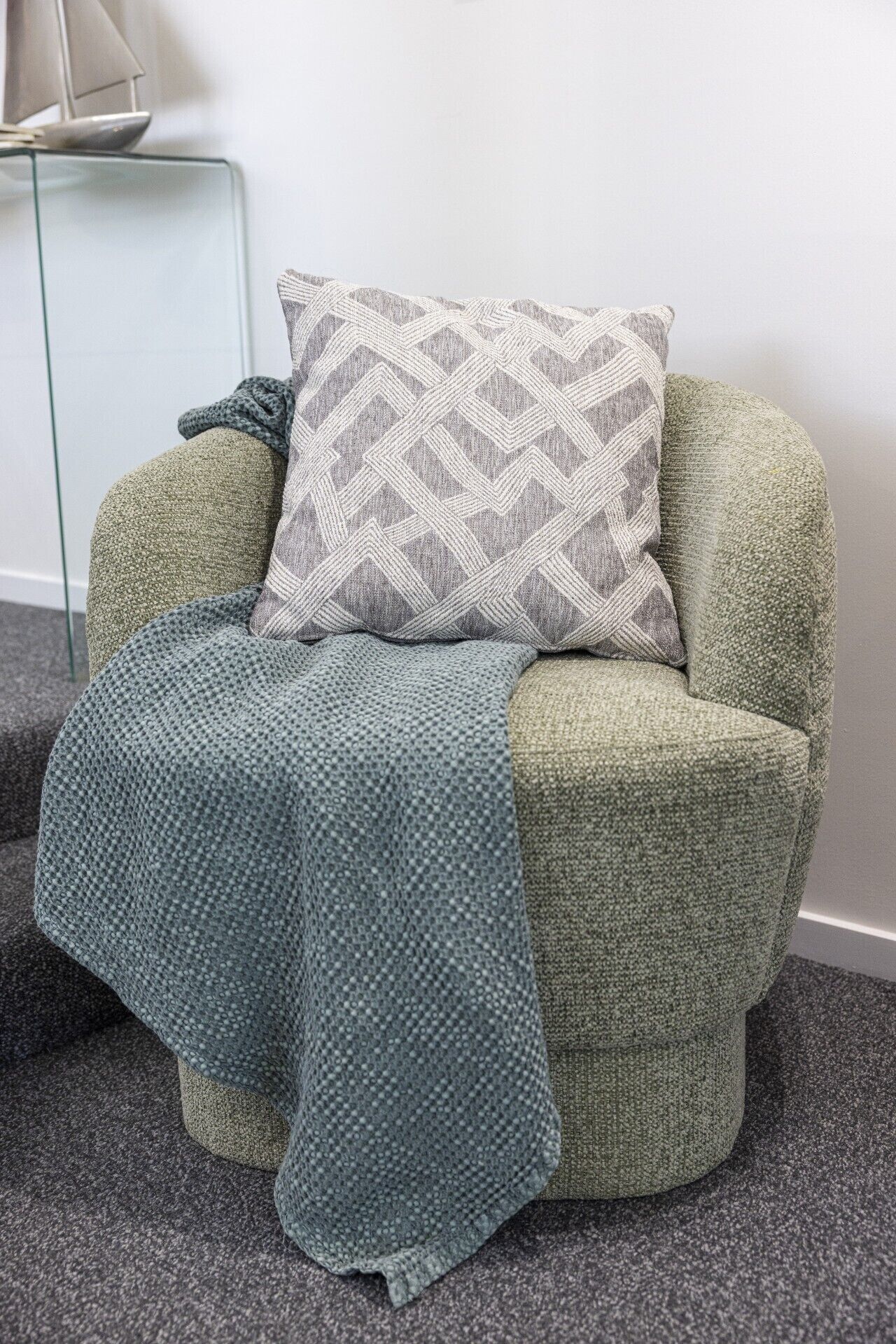 A corner armchair with a patterned throw blanket and a geometric pillow.