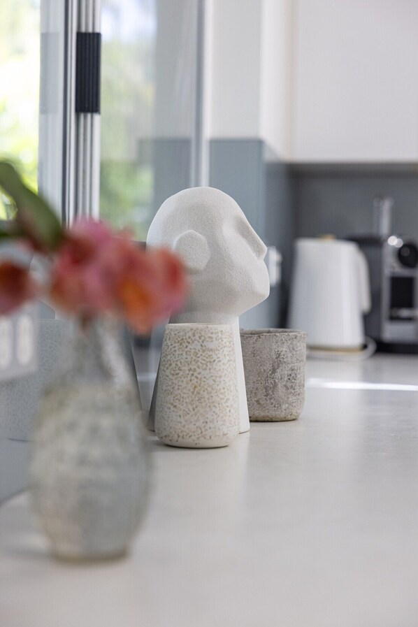 Una encimera de cocina con un florero de flores, dos tazas de cerámica con motas y un electrodoméstico blanco al fondo.