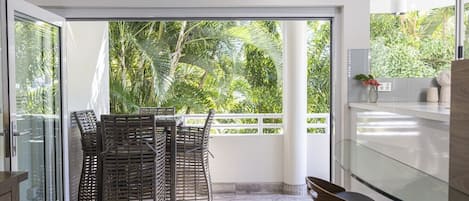 Una cocina moderna con puerta de cristal que da a un balcón con mobiliario de mimbre y vistas a exuberante vegetación.