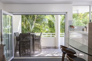Una cocina moderna con puerta de cristal que da a un balcón con mobiliario de mimbre y vistas a exuberante vegetación.