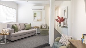 A modern living room with a grey sofa, a small round table, and a staircase leading to another level. - BeachLuxe @ Sunseeker, Sublime Tropical Apartment (Port Douglas)